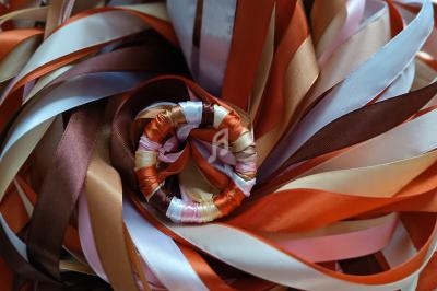 Rubans colorés enroulés en spirale, dans des tons orange, marron, blanc et rose, posés sur un fond en tissu tressé.
