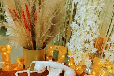 Téléphone vintage blanc posé sur une table rouge, entouré de fleurs blanches, pampas et lettres lumineuses dorées.