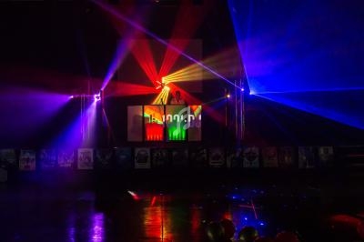 Un DJ mixe sur une scène éclairée par des faisceaux lumineux colorés dans une ambiance sombre.