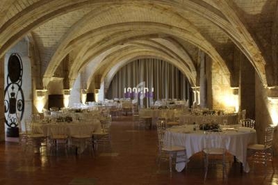 Salle voûtée en pierre avec tables rondes dressées pour un événement, éclairage chaleureux et rideaux en fond.