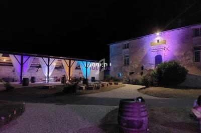 Cour extérieure éclairée de nuit avec des bâtiments en pierre, des lumières colorées et des espaces de détente aménagés.