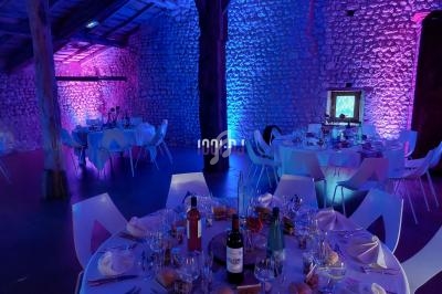 Salle de réception en pierre éclairée par des lumières colorées, avec tables dressées pour un repas festif.
