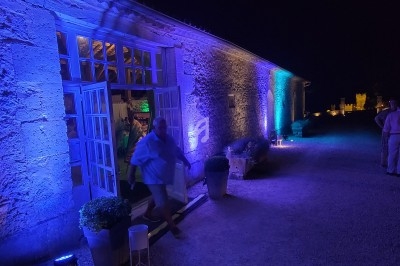 Façade en pierre éclairée de lumières bleues, avec une porte ouverte laissant entrevoir un intérieur illuminé.