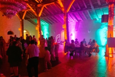 Salle en pierre éclairée par des lumières colorées, avec des invités dansant et discutant autour de tables.
