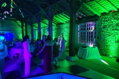 Des personnes dansent dans une salle en pierre éclairée par des lumières vertes et violettes lors d'un événement festif.
