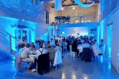 Salle de réception en pierre avec invités assis à des tables rondes, éclairage bleu et décoration suspendue.