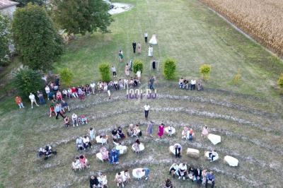 Vue aérienne d'un rassemblement en plein air, des personnes assises en demi-cercle sur une pelouse entourée d'arbres.