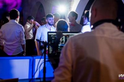 Un DJ anime une soirée dansante avec des invités discutant et dansant sous des lumières colorées.