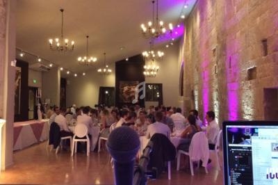 Salle de réception avec invités assis à des tables, éclairage tamisé et décorations lumineuses, vue depuis un micro.