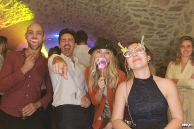 Des personnes souriantes posent avec des accessoires humoristiques dans une ambiance festive sous une voûte en pierre.