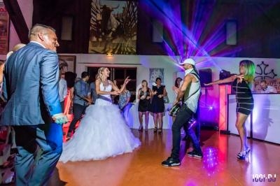 Des invités dansent lors d'une réception de mariage avec éclairages colorés et un musicien jouant de la guitare.