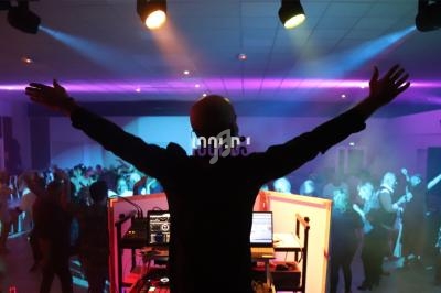 Un DJ de dos anime une soirée dansante avec des jeux de lumière colorés et une foule en mouvement.