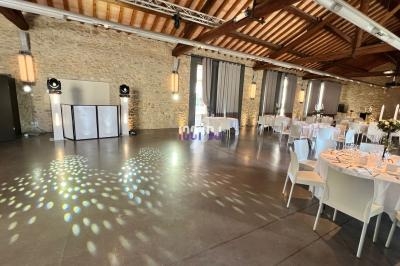 Salle de réception avec murs en pierre, tables dressées, éclairage tamisé et piste de danse illuminée.