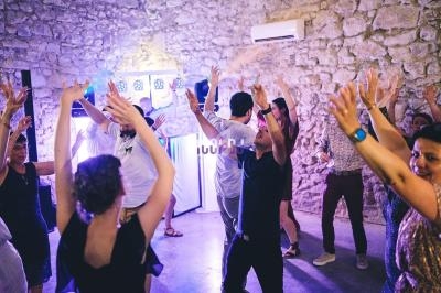 Des personnes dansent joyeusement dans une salle en pierre éclairée par des lumières colorées.