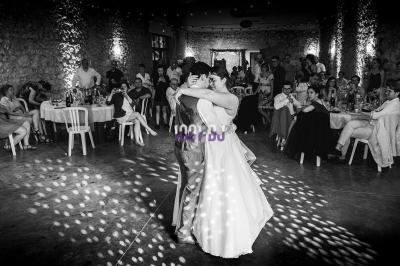 Un couple danse au centre d'une salle en pierre éclairée, entouré d'invités assis et debout.