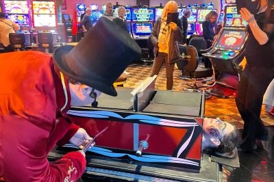 Un homme déguisé en magicien près d'un cercueil rouge dans un casino, entouré de spectateurs.