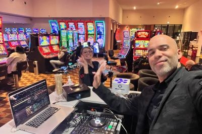 Un DJ souriant devant son équipement dans une salle de jeux avec des machines à sous en arrière-plan.