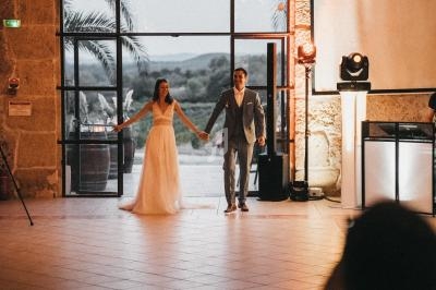 Un couple en tenue de mariage entre dans une salle éclairée, avec une vue sur l'extérieur au crépuscule.