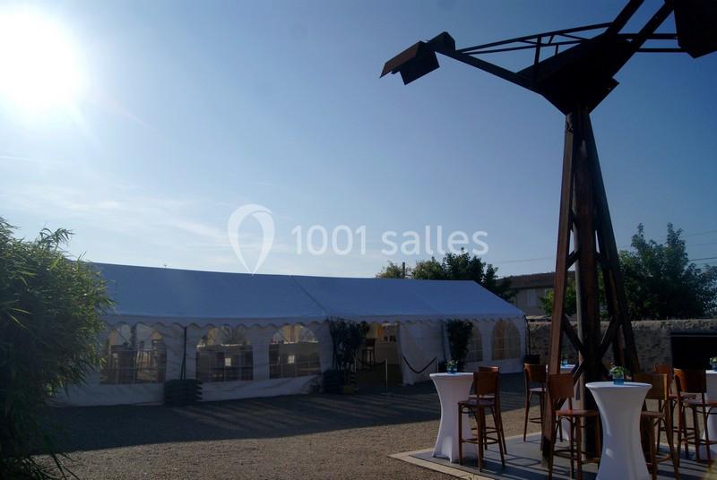 Tente blanche installée en extérieur par temps ensoleillé, avec tables hautes et chaises en premier plan.