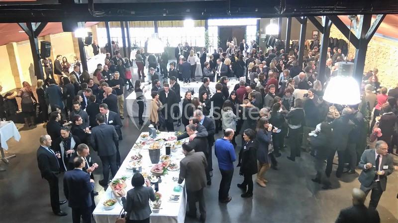 Groupe de personnes rassemblées dans une salle pour un événement, avec des tables de buffet au centre.