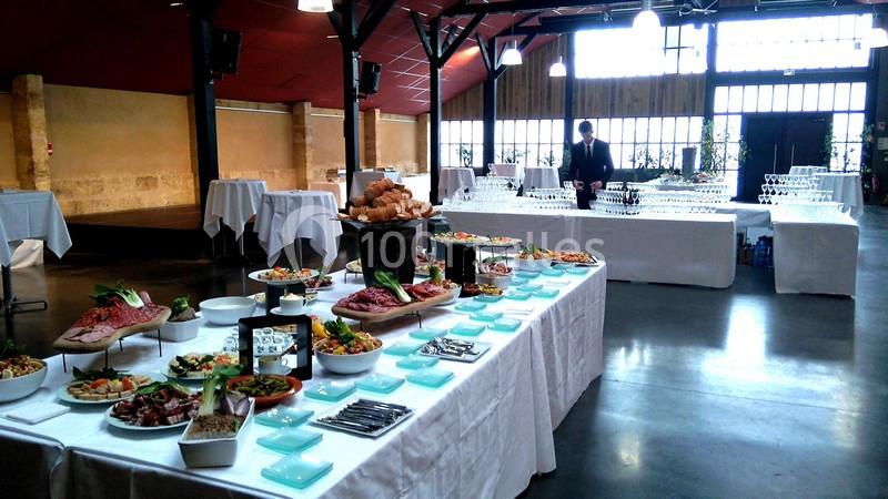 Buffet varié avec plats froids, pains et verrines, disposé dans une grande salle lumineuse avec tables dressées.