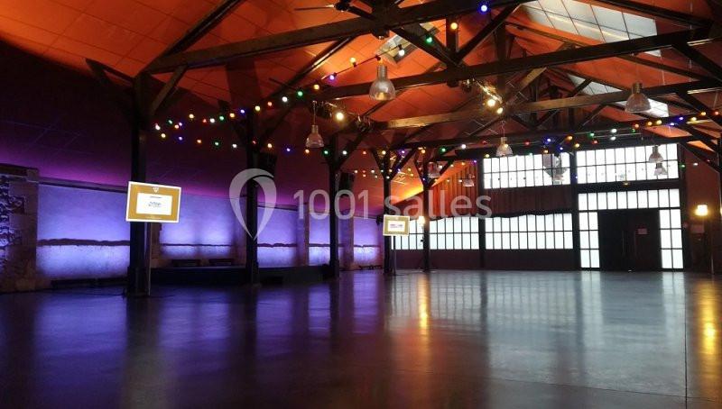 Salle spacieuse avec plafond en bois, éclairage coloré et écrans allumés, prête pour un événement.