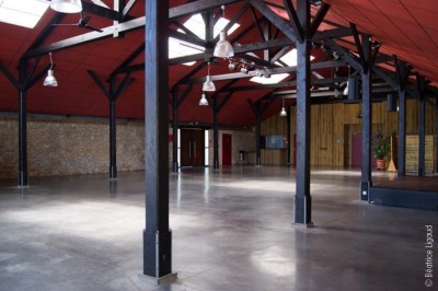 Bâtiment en bois avec une clôture métallique et un panneau indiquant ’La Forge’, entouré de végétation.