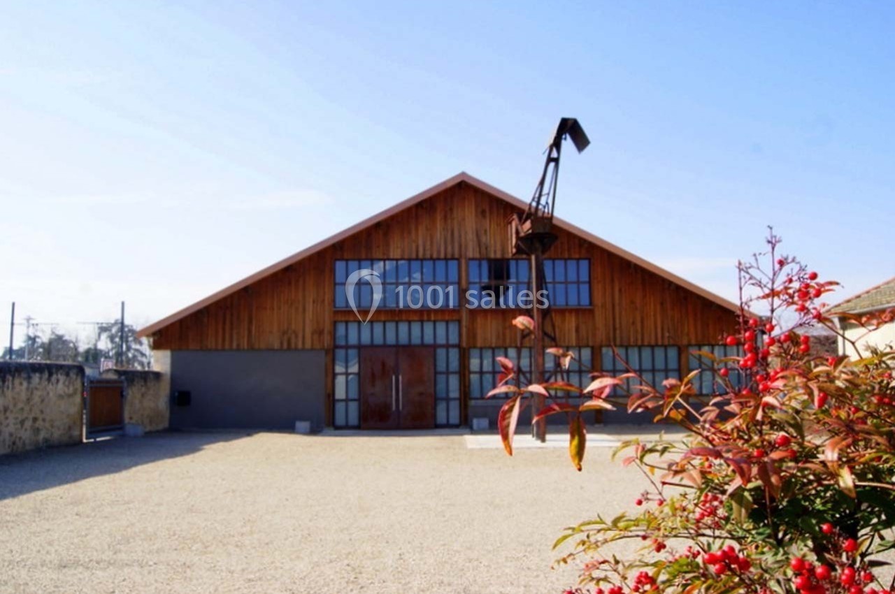 Bâtiment en bois avec de grandes baies vitrées, une grue ancienne devant et des arbustes rouges au premier plan.