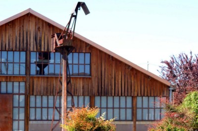 Bâtiment en bois avec une clôture métallique et un panneau indiquant ’La Forge’, entouré de végétation.