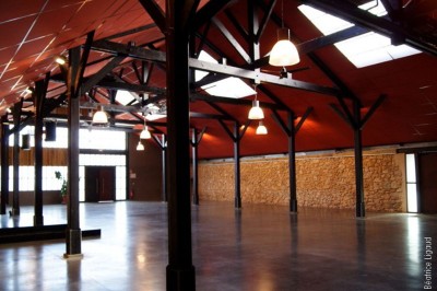 Bâtiment en bois avec une clôture métallique et un panneau indiquant ’La Forge’, entouré de végétation.