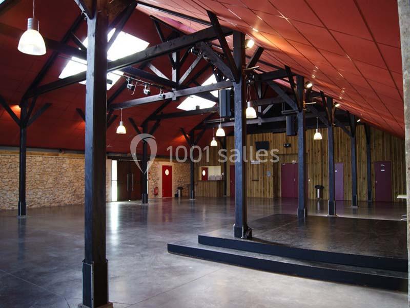 Salle spacieuse avec charpente en bois apparente, murs en pierre et bois, sol en béton, et plafond rouge.