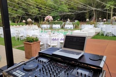 Table de mixage et ordinateur portable installés en extérieur, avec des tables décorées pour un événement sous des…