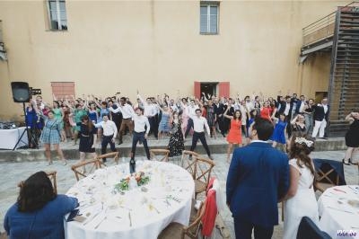 Groupe de personnes dansant en extérieur lors d'une réception, devant un bâtiment beige avec des tables dressées.
