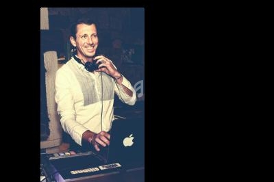 Homme souriant utilisant un ordinateur portable et un équipement de DJ dans un environnement intérieur.