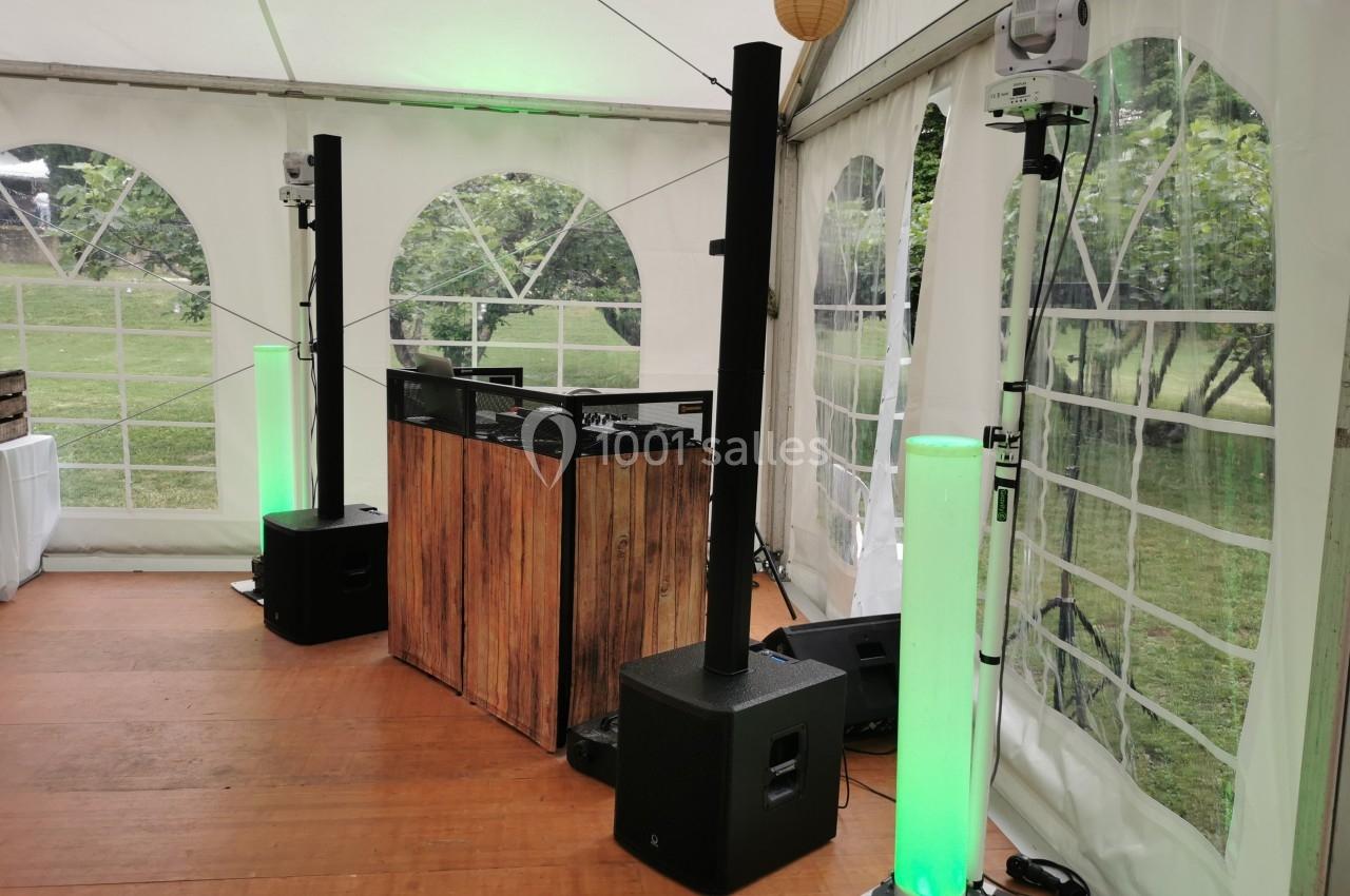 Équipement de sonorisation et éclairage installé sous une tente avec vue sur un jardin à travers les fenêtres.