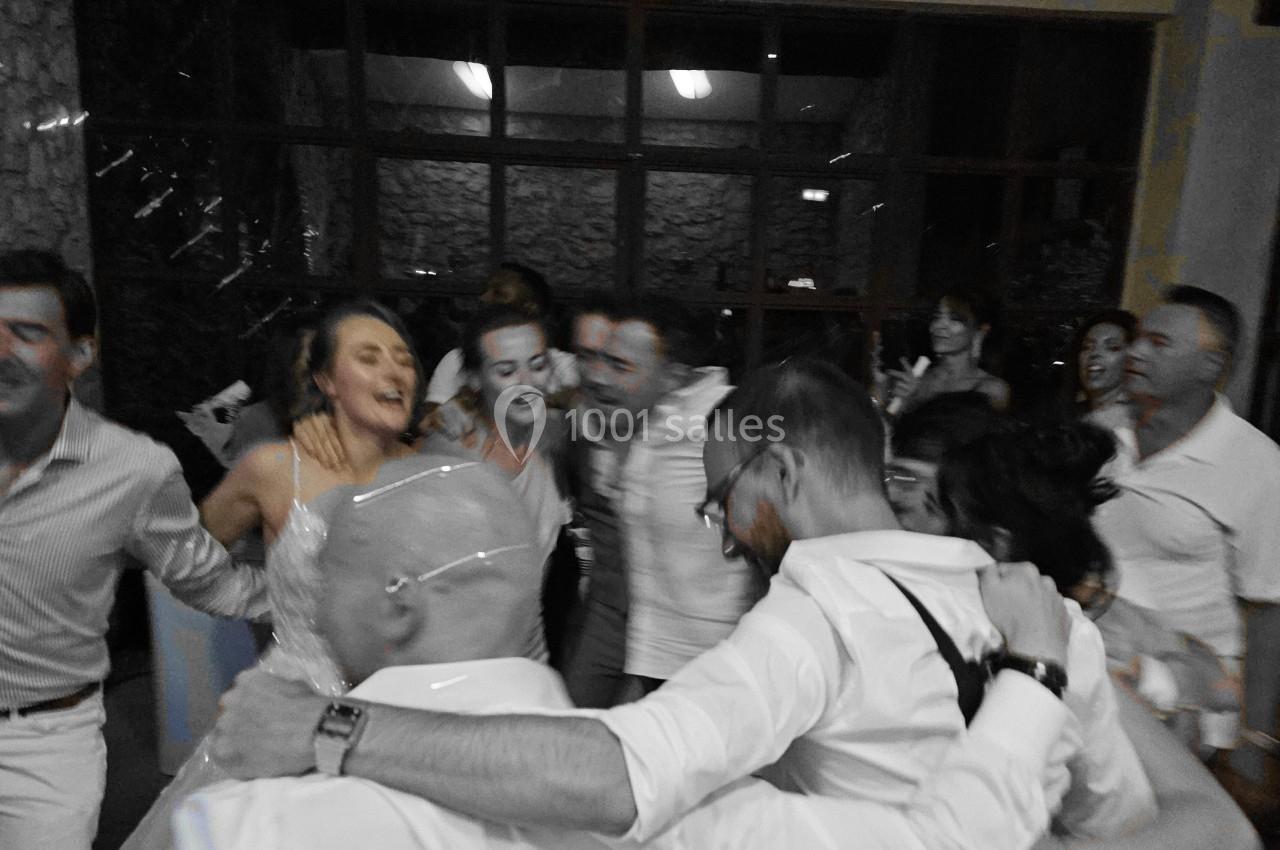 Des personnes dansent en cercle, souriantes et enlacées, dans une ambiance festive à l'intérieur d'une salle.