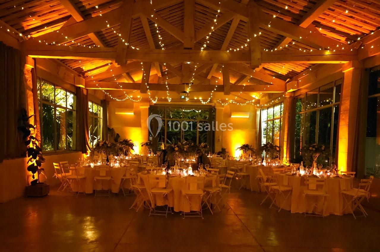 Salle de réception décorée avec des guirlandes lumineuses, des tables rondes dressées et une ambiance chaleureuse.