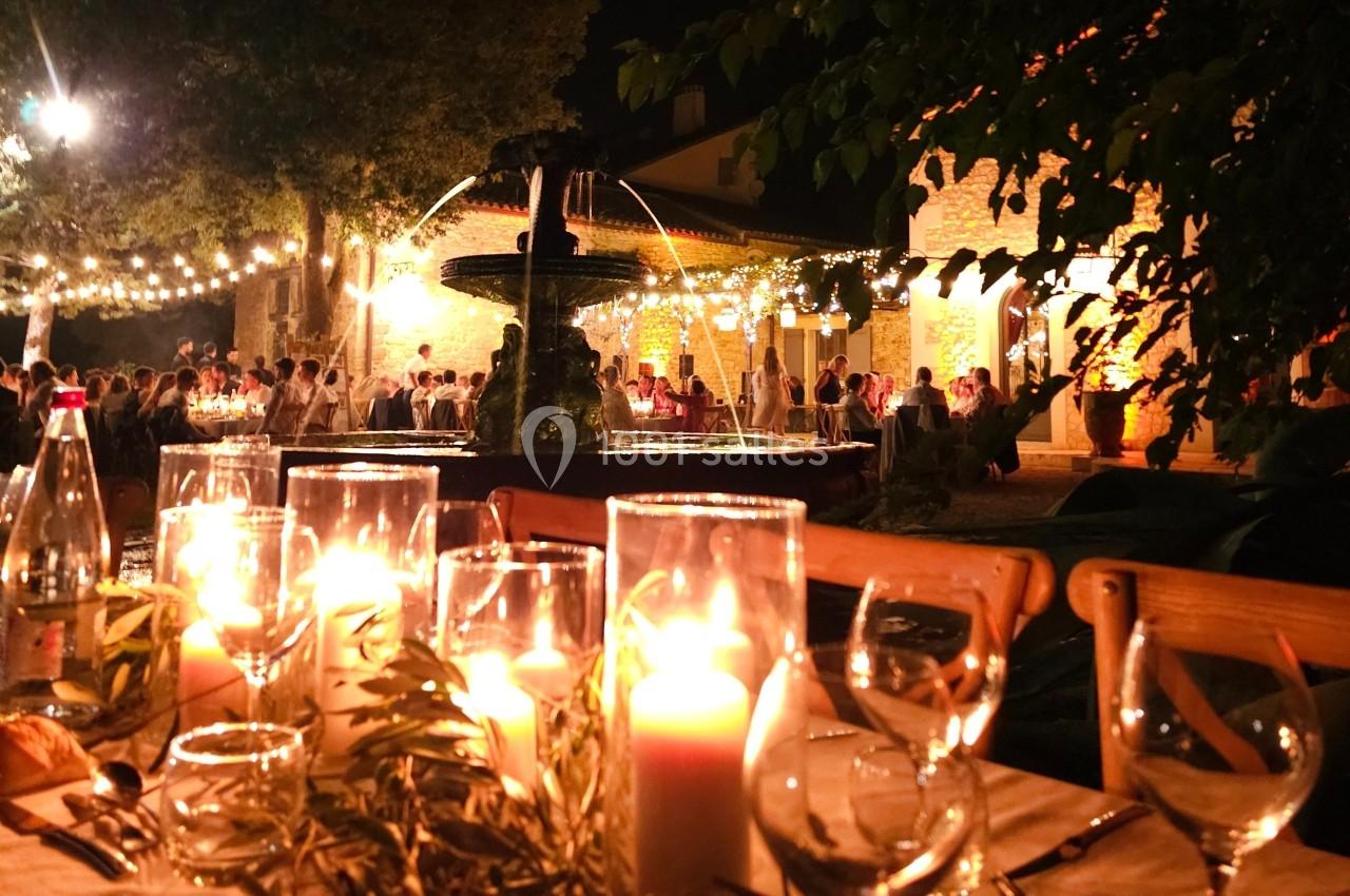Table décorée avec des bougies allumées en premier plan, devant une fontaine éclairée et une réception en soirée.