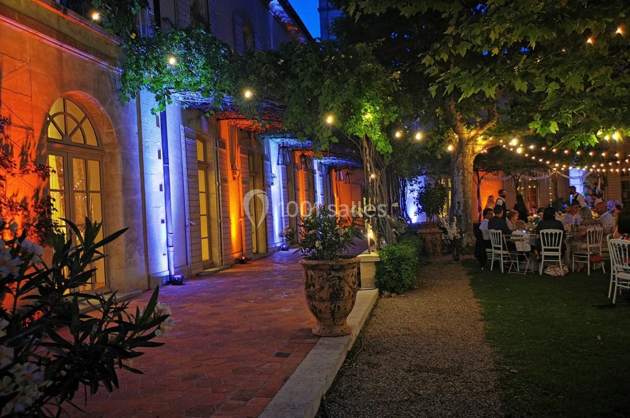 Cour extérieure éclairée par des guirlandes lumineuses, avec des tables dressées et une façade en pierre illuminée.