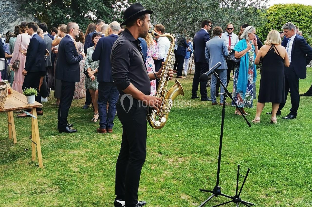 Un musicien jouant du saxophone lors d'un événement en plein air, entouré de personnes discutant.