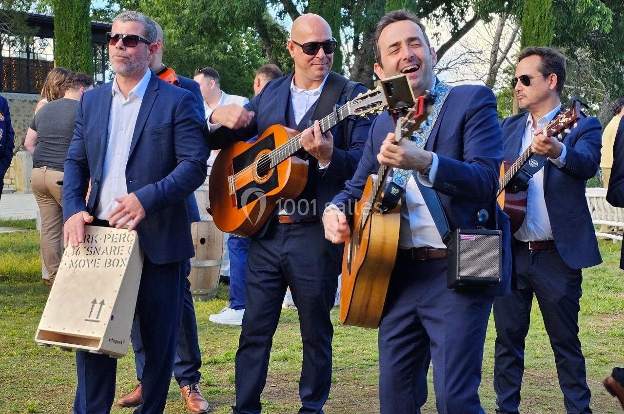 Quatre musiciens en costume jouent de la guitare et du cajón en extérieur lors d'un événement.