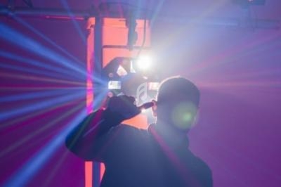 Silhouette d'une personne pointant vers une lumière vive, entourée de rayons colorés dans une ambiance sombre.