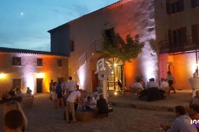 Cour intérieure éclairée au crépuscule, avec des invités assis ou debout autour de tables et décorations lumineuses.