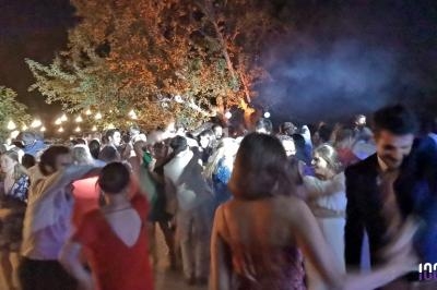 Des personnes dansent en soirée en plein air, éclairées par des guirlandes lumineuses et des projecteurs.