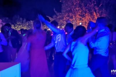 Des personnes dansent en soirée en plein air, éclairées par des lumières colorées dans une ambiance festive.