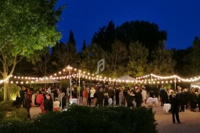 Groupe de personnes rassemblées en soirée dans un jardin éclairé par des guirlandes lumineuses.