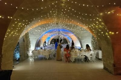 Salle voûtée décorée de guirlandes lumineuses, avec des tables dressées et des invités assis ou debout.
