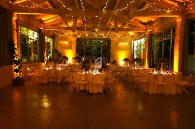 Salle de réception décorée avec des guirlandes lumineuses, tables rondes dressées et ambiance chaleureuse.