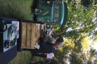 Un stand en plein air avec un camion vintage, des platines de DJ et des personnes se servant de la nourriture.