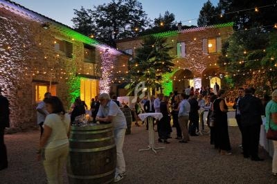 Personnes réunies dans une cour en soirée, éclairée par des guirlandes lumineuses et entourée de bâtiments en pierre.